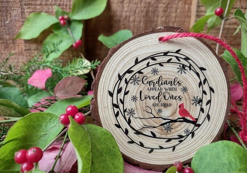 A wood-slice, rustic ornament with a vine, snowflakes, a cardinal, and the phrase "cardinals appear when loved ones are near."